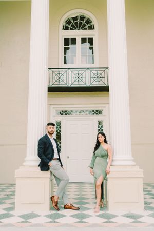 Couple posing between white columns with checkered floor in elegant architectural setting.
