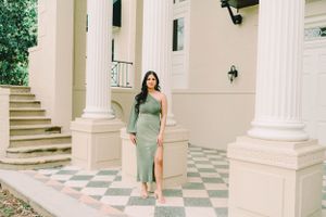 Elegant architectural setting with white columns, checkered floor, and greenery in background.