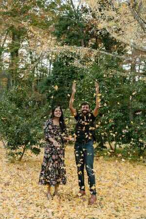 Three people throw autumn leaves in the air while enjoying a playful moment in a park setting with golden foliage.