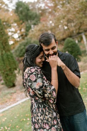 A couple shares a tender moment together in an outdoor autumn setting with fallen leaves and trees in the background.