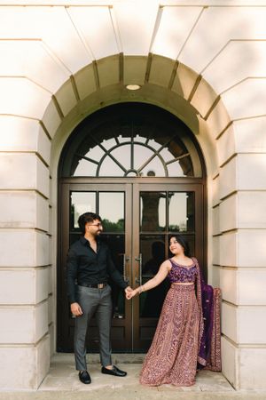 Couple poses playfully in formal attire at an ornate arched entrance.