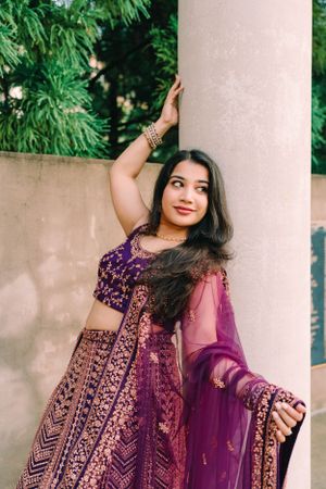 Elegant purple and gold embroidered lehenga outfit photographed against garden backdrop.