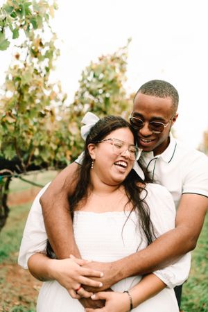 Joyful couple laughing together in casual attire among vineyard rows.