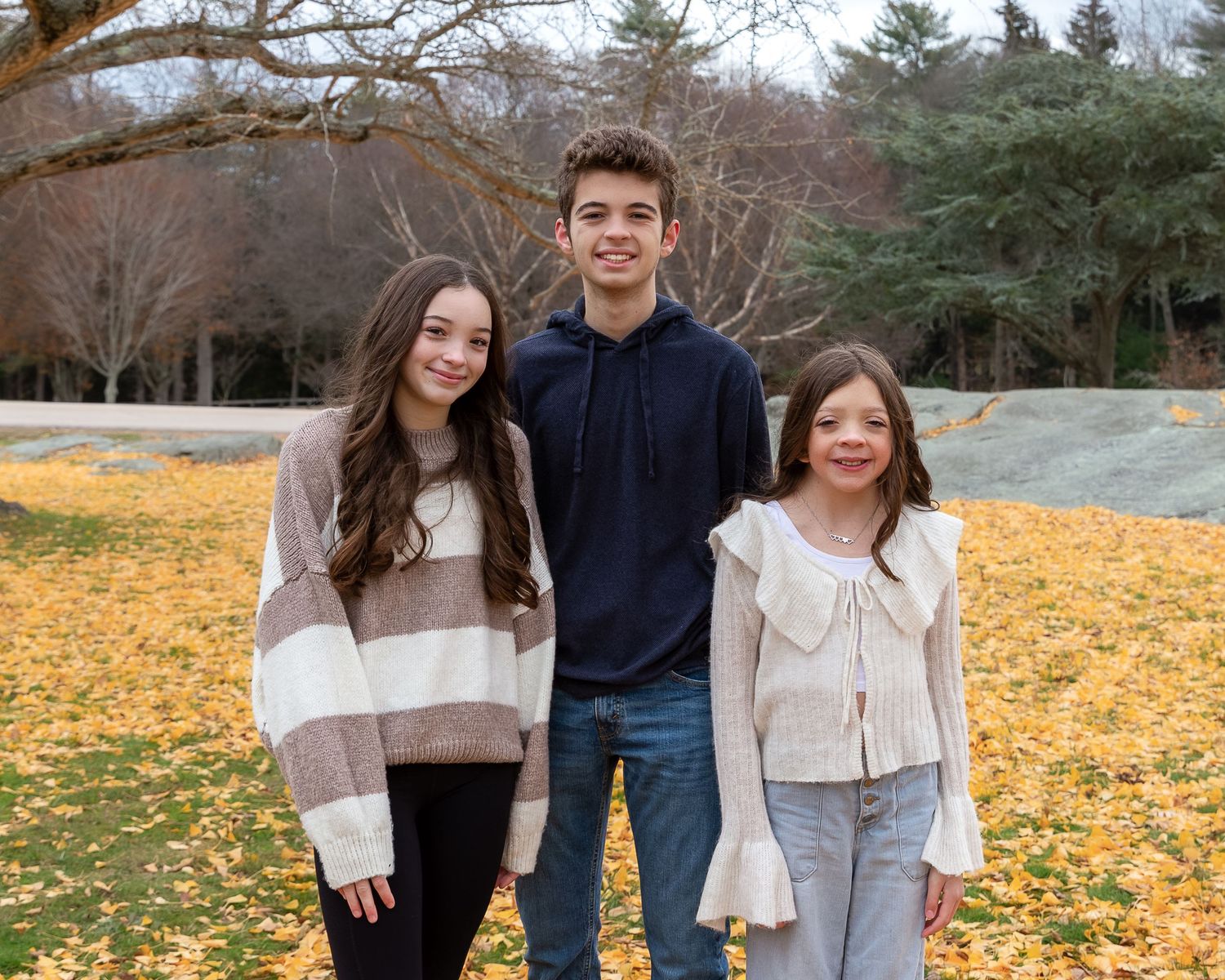 teen boy, preteen girl and young girl, all in a hug smiling towards camera against brown backdrop