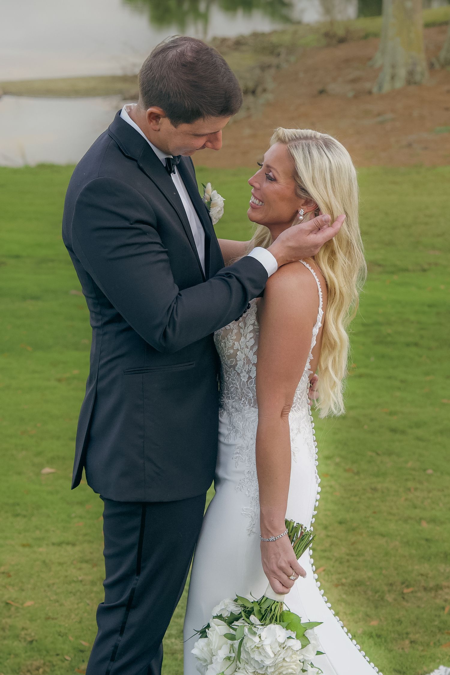 A couple share an intimate moment on their wedding day on a green lawn while wearing formal attire.