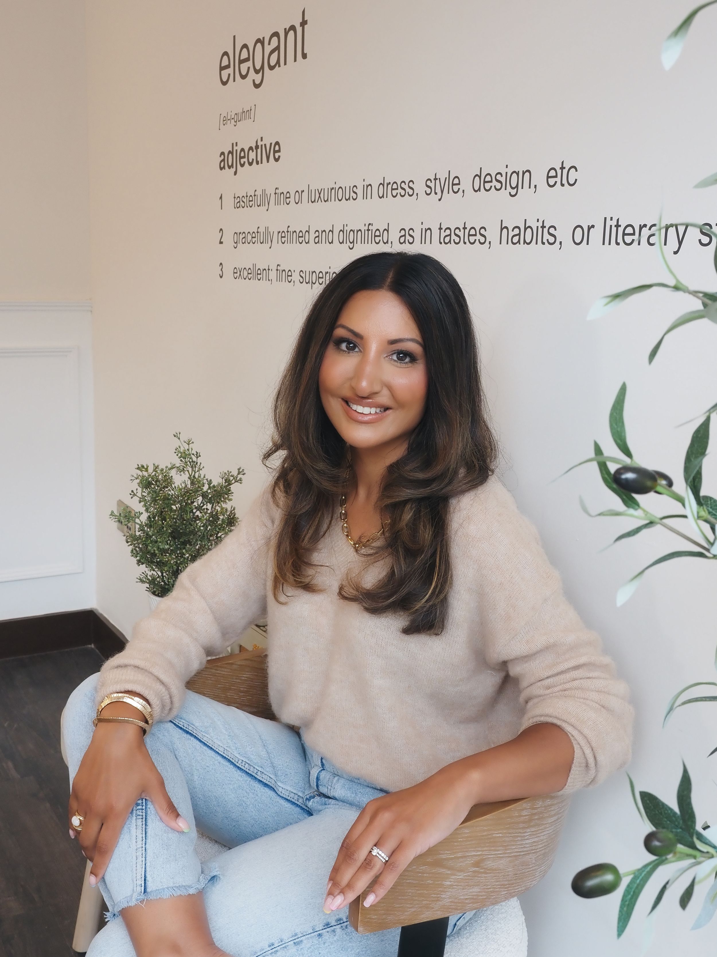 A person in a beige sweater and jeans sits relaxed in a room with elegant typography wall decor and greenery.