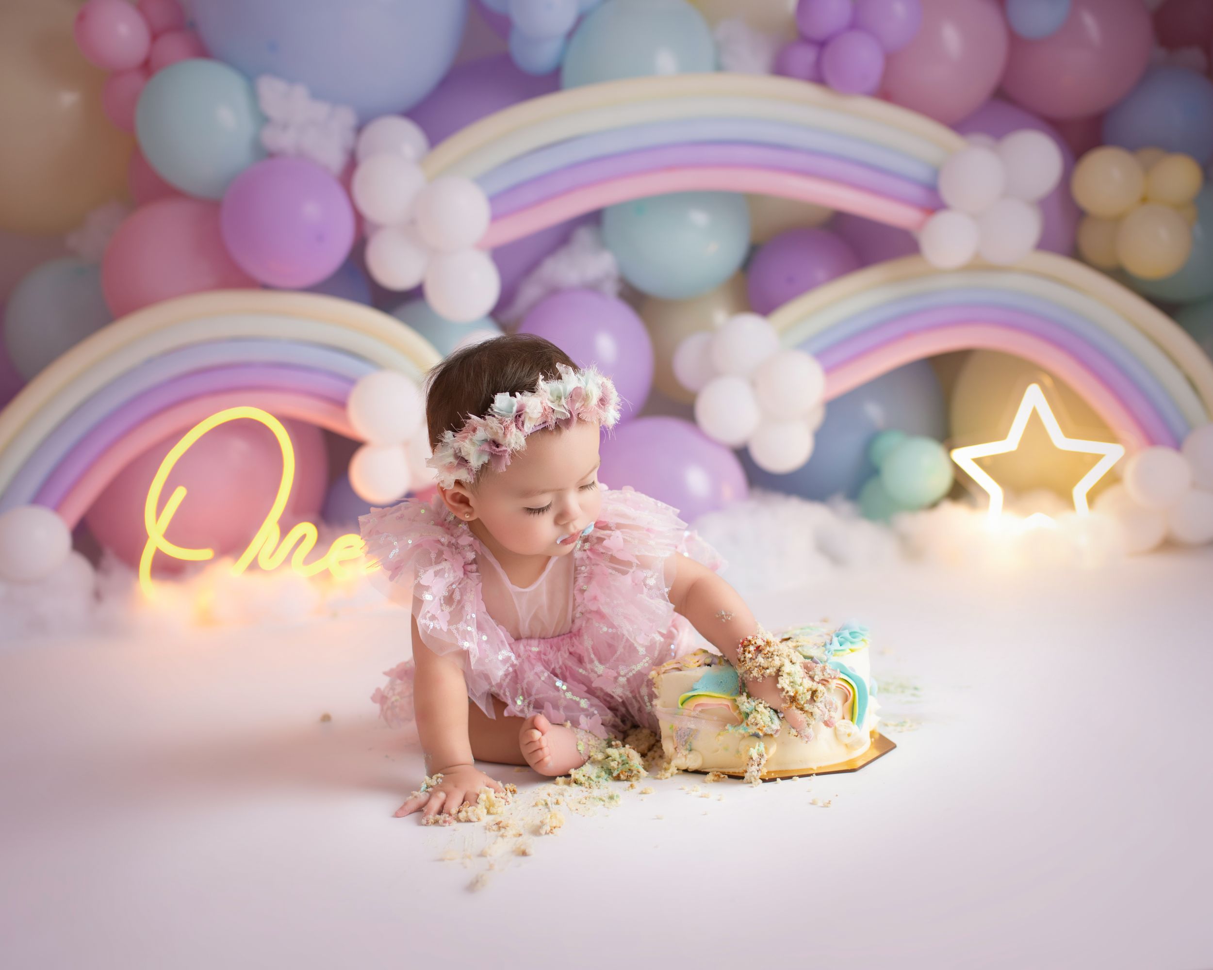 Sweet cake smash portrait with pastel decorations and illuminated rainbow background.