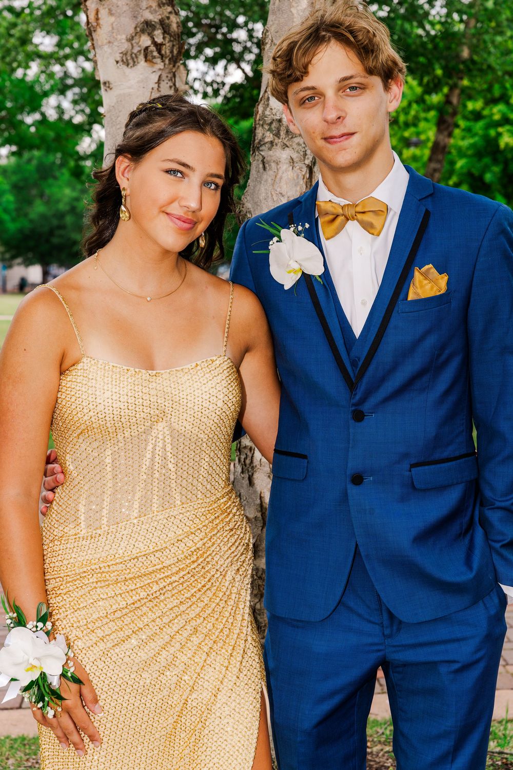 Smiling prom couple in gold sequin dress and blue suit with gold bow tie.