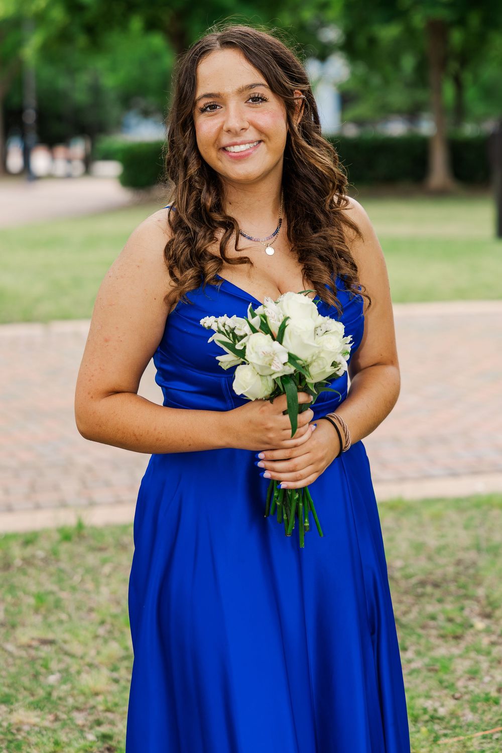 Young woman in royal blue strapless prom dress holding white flower bouquet.