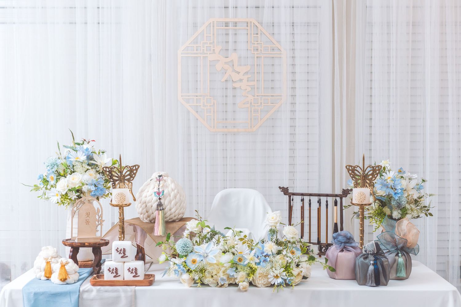 Elegant dessert table decorated with pink and blue floral arrangements, cakes, and vintage-style decor.