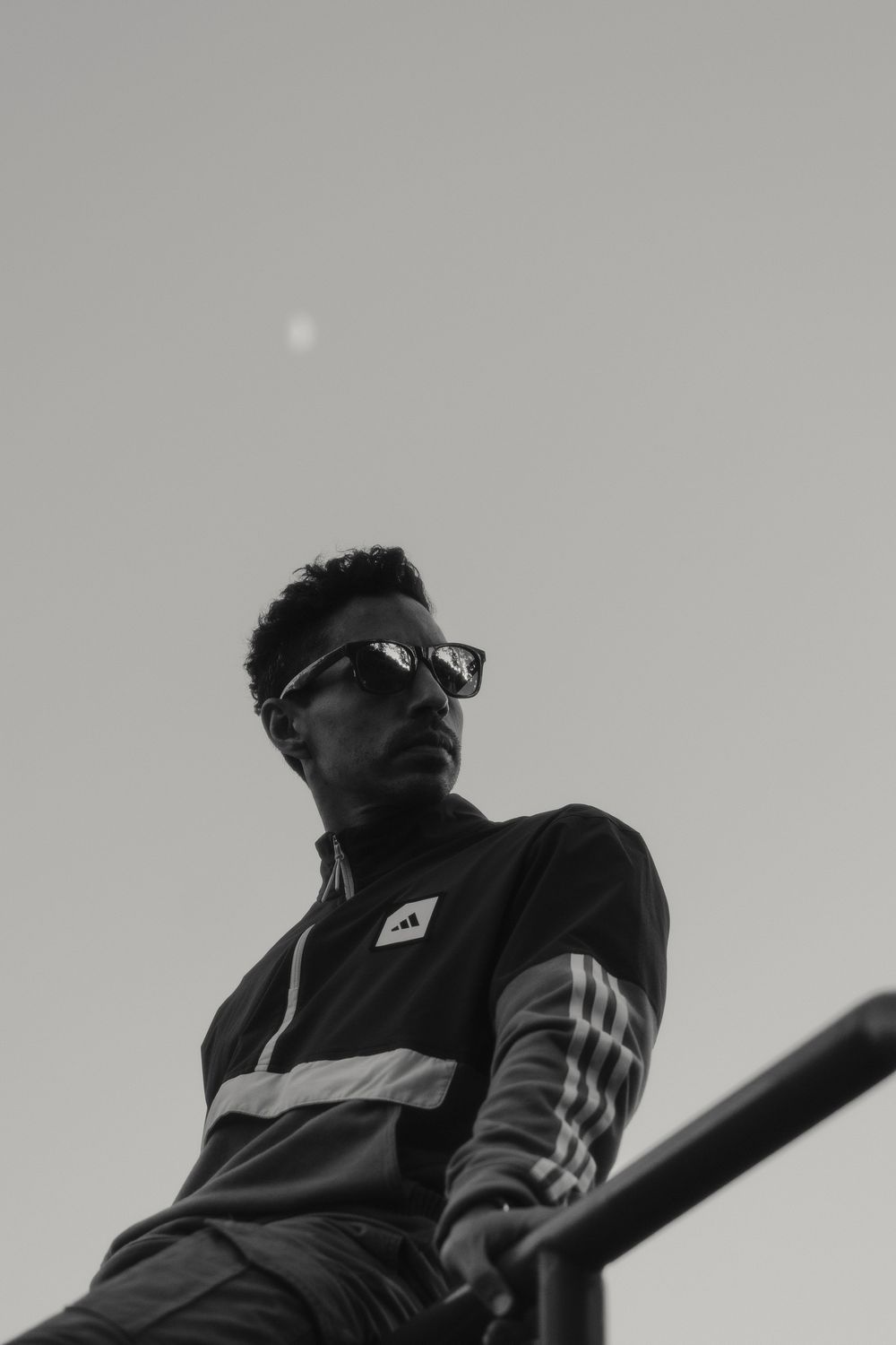 Low angle black and white portrait of a person wearing sunglasses and sportswear against a light sky.