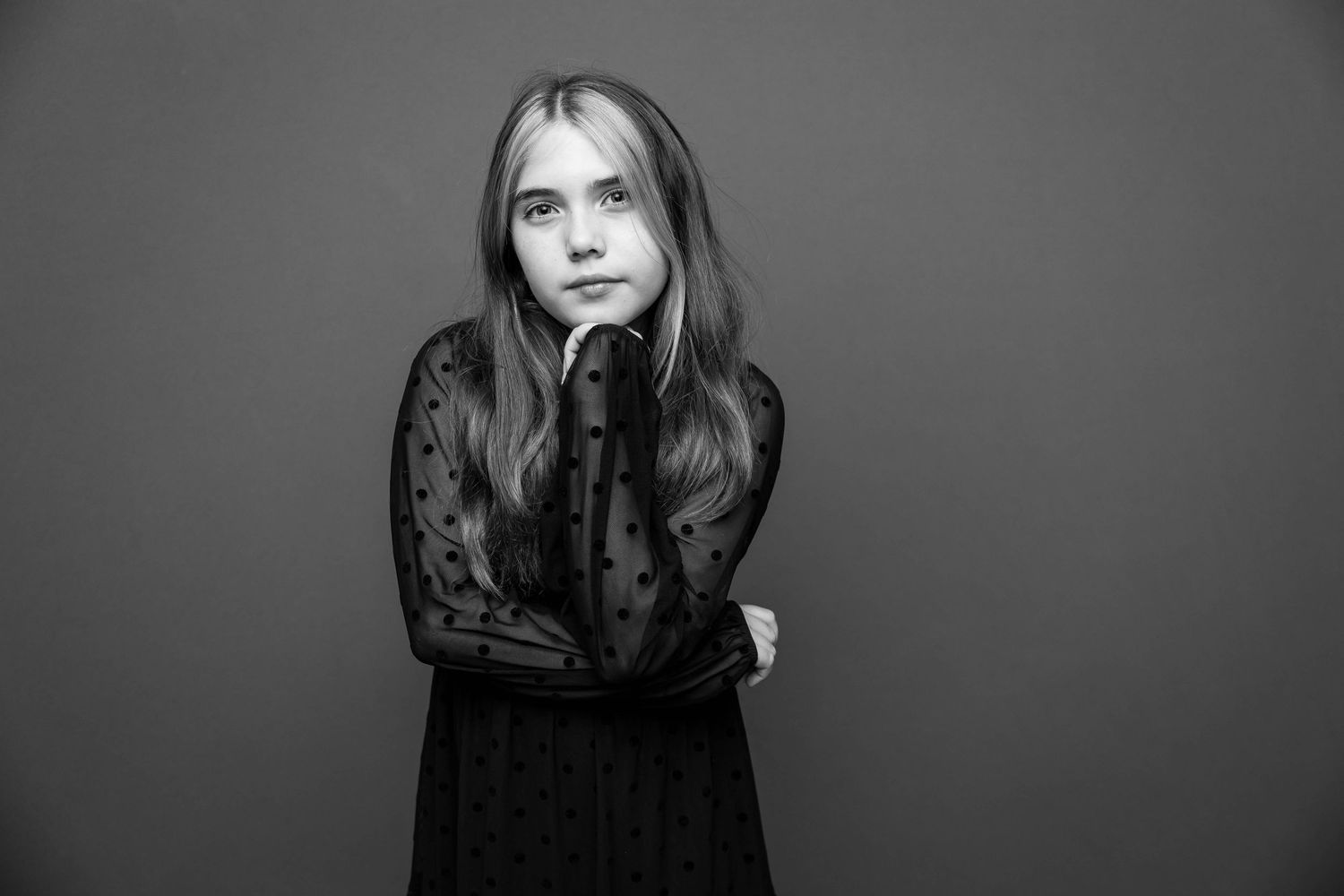 Black and white fashion portrait of someone in a long sleeve lace dress against a dark background.