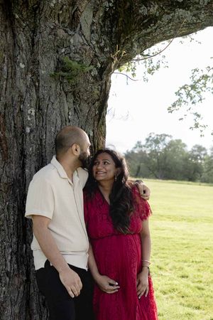 Couple enjoying a romantic moment together under a large tree in a sunny meadow.