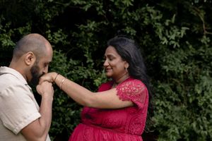 A sweet outdoor moment captured between two people, one wearing red lace and the other in beige, against green foliage.