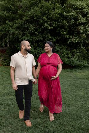 Two people share an intimate moment while walking through lush green grass in summer attire and casual clothing.