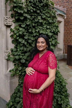 A person wearing a red lace dress poses outdoors against a brick wall with climbing ivy.