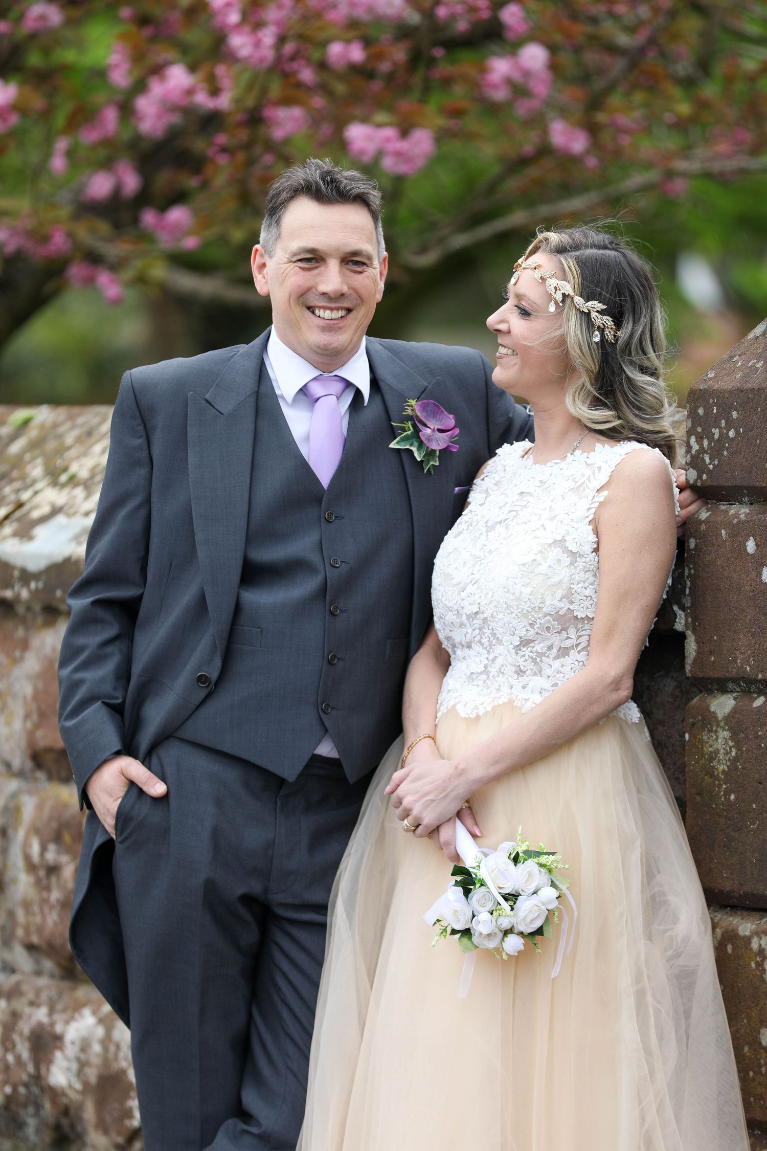 Bride and groom share a joyful moment against a backdrop of pink cherry blossoms.