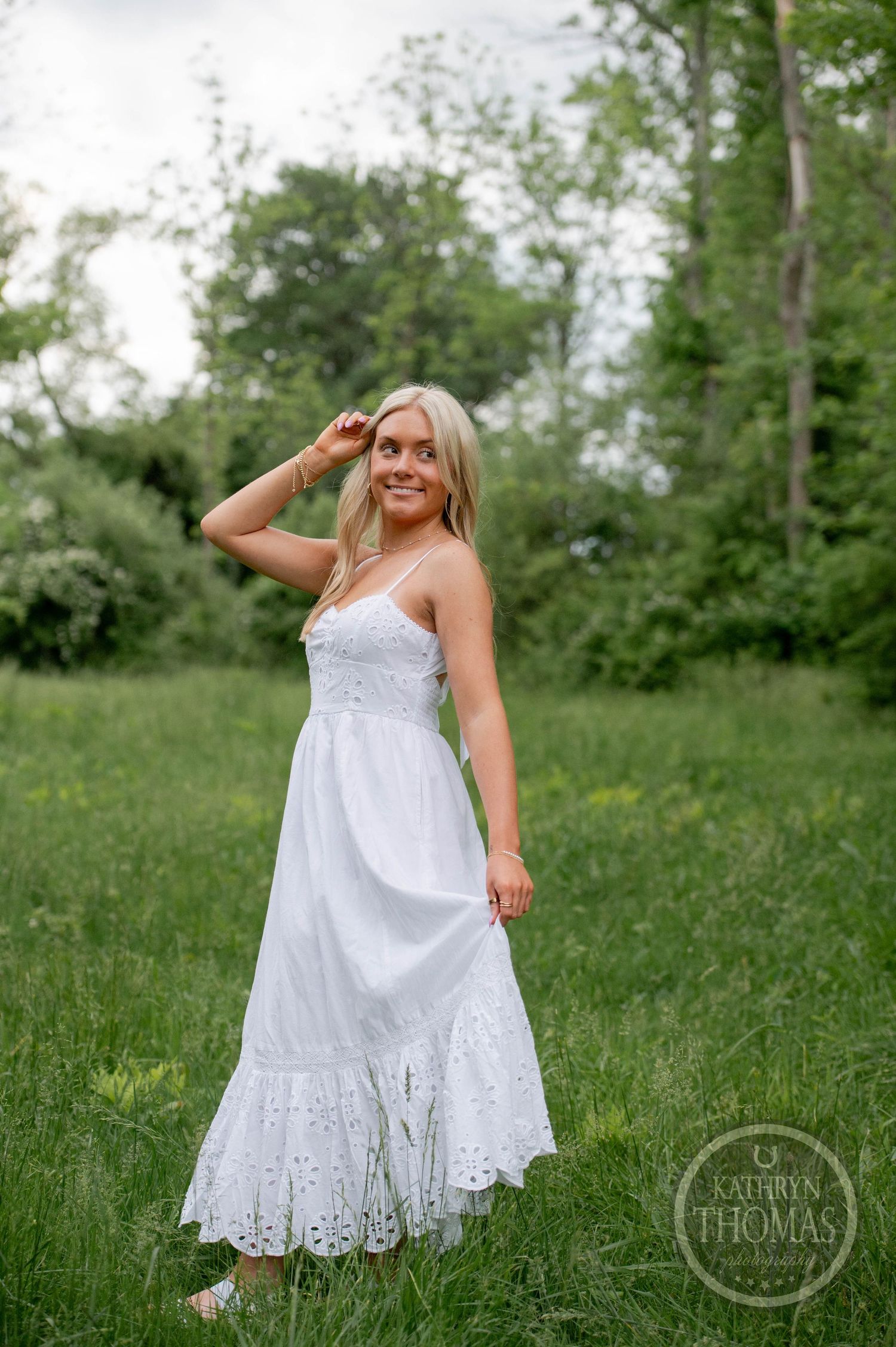 A person in a flowing white eyelet lace maxi dress stands in a green meadow on a summer day.