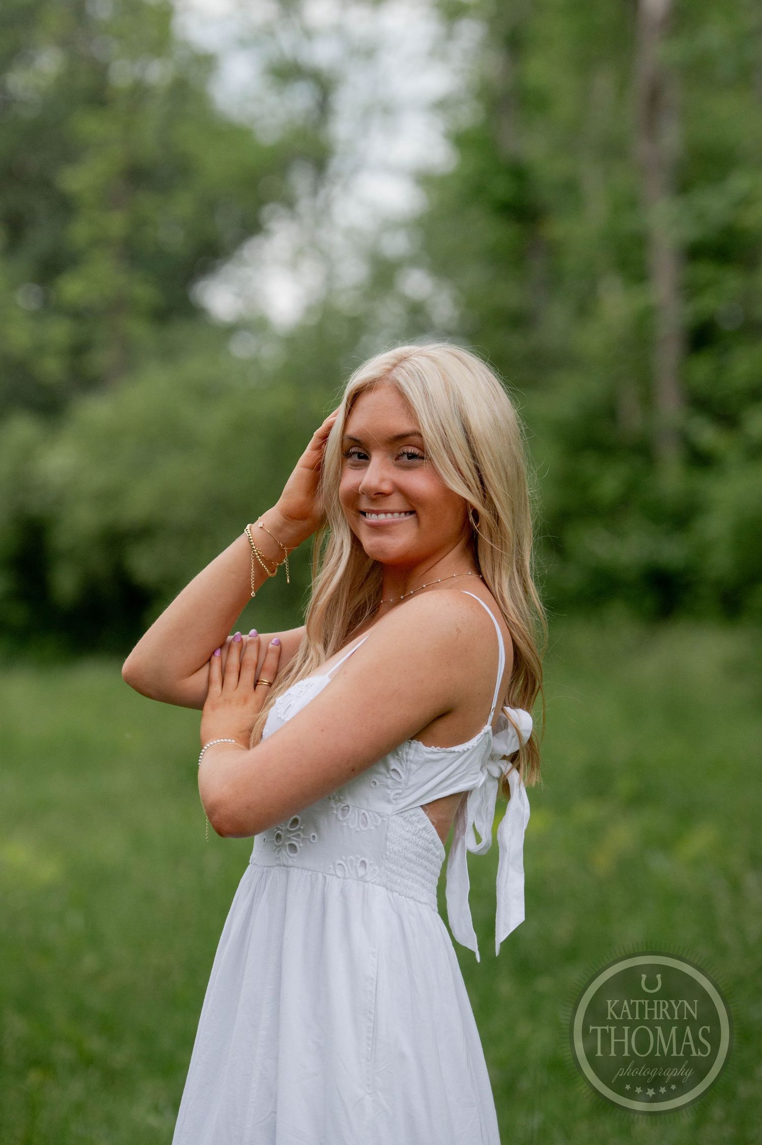 Black and white portrait of someone in a light summer dress with ribbon details, smiling outdoors in a natural setting.