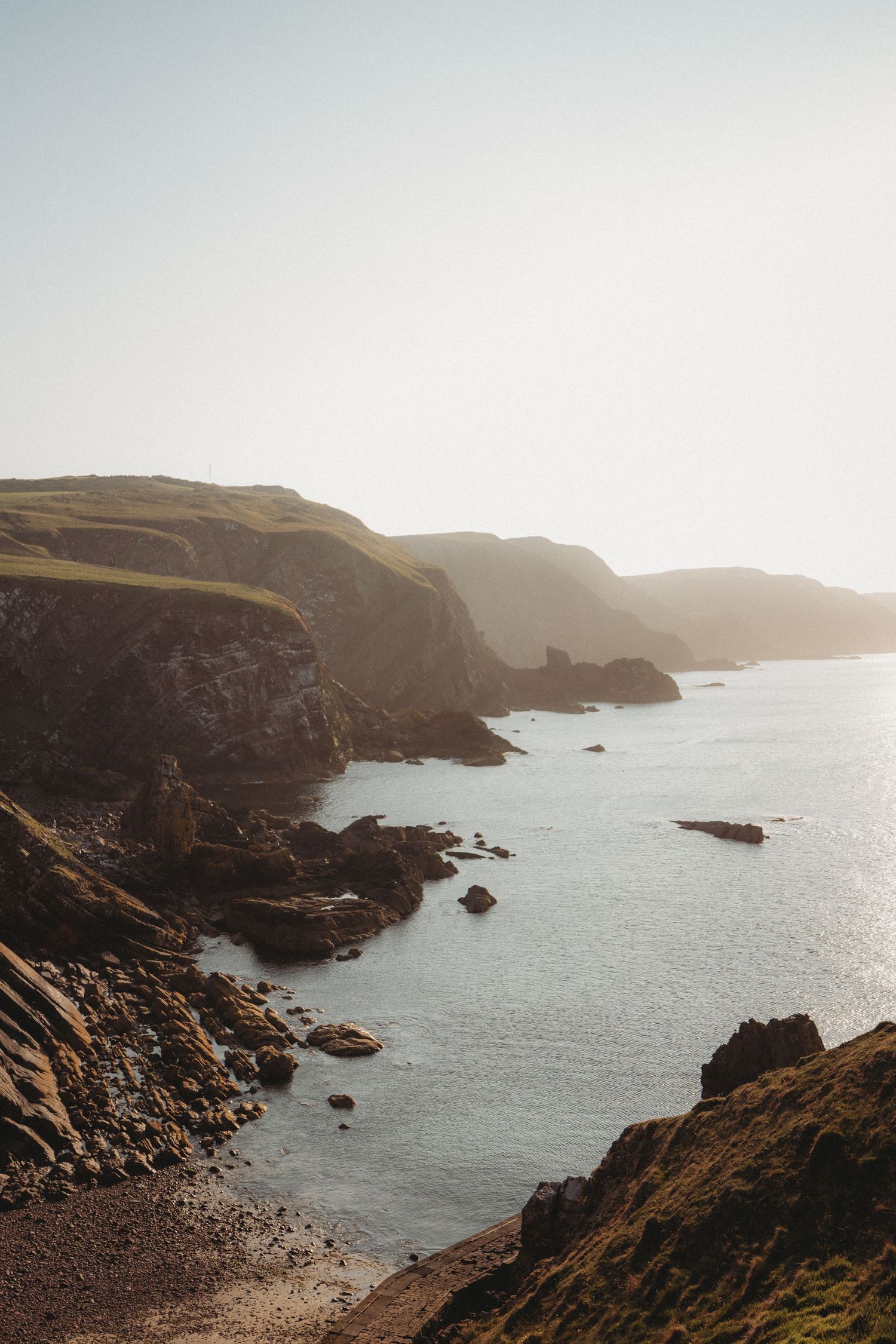 Dramatic coastal cliffs and rocky shoreline along a misty coastline under moody cloudy skies.