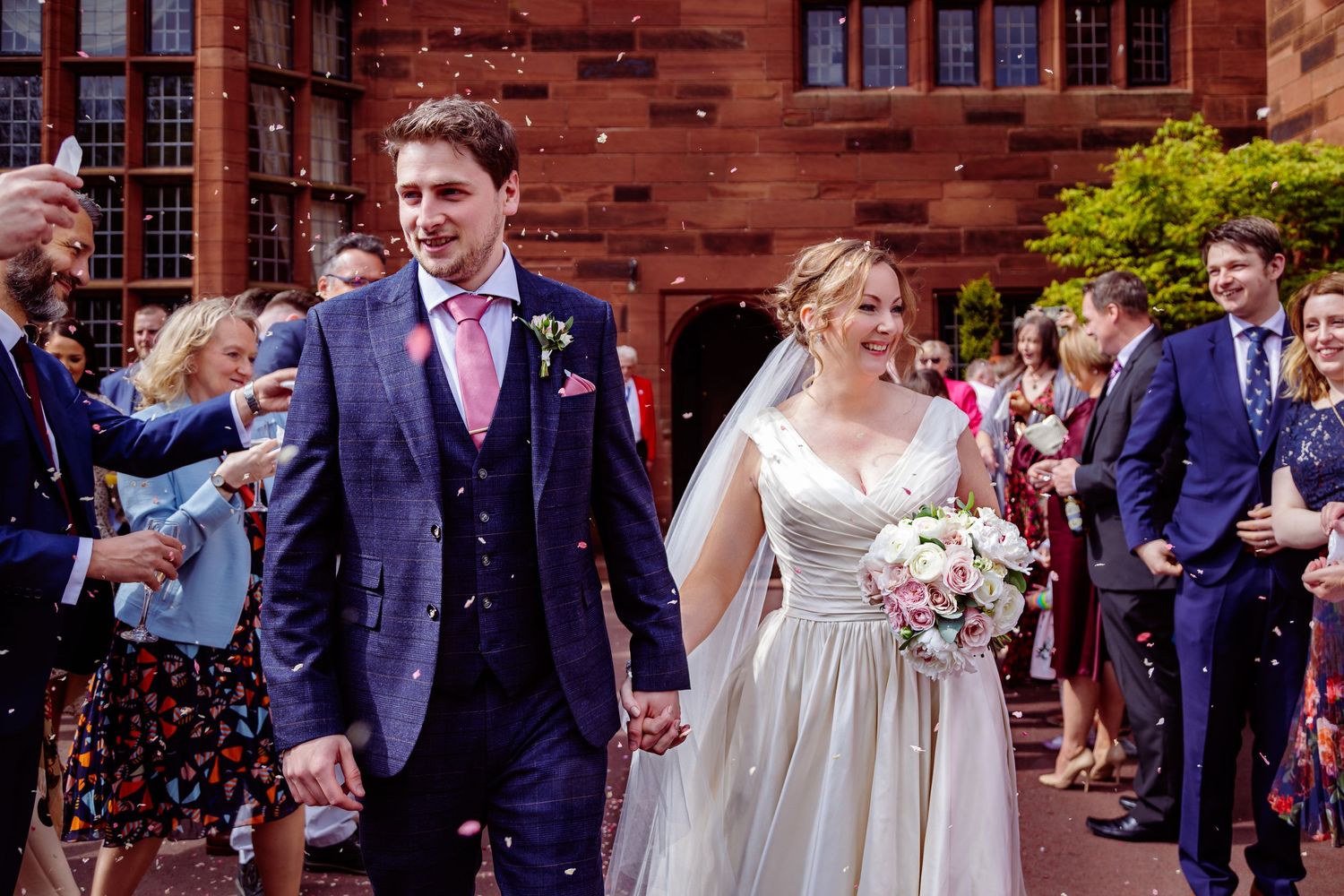 A happy couple walks together through falling confetti in a black and white wedding scene.