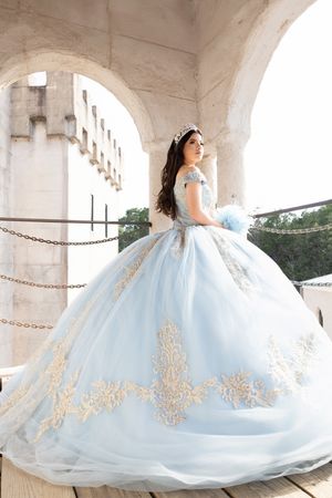 Elegant light blue ball gown with gold embellishments shown in a series of poses under stone colonnade.