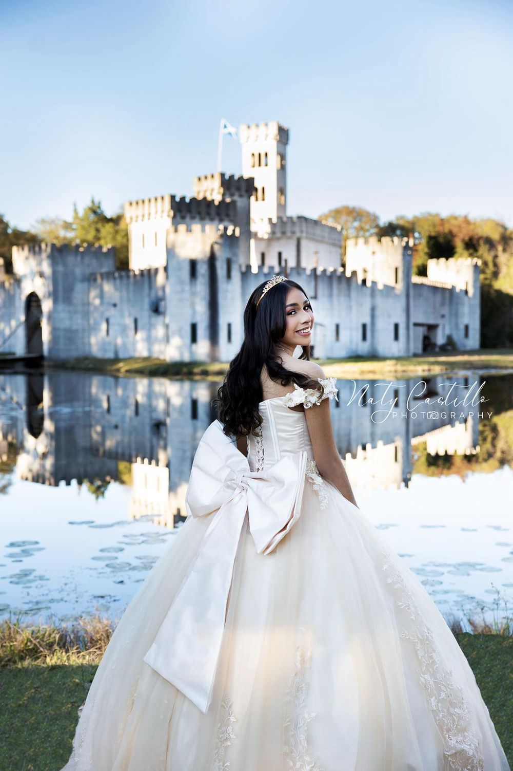 Romantic bridal portrait in white gown with castle and reflective lake in background.