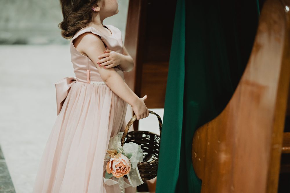 Person in blush pink dress holding floral basket against green background.