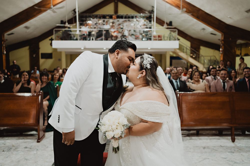 Couple shares intimate kiss during wedding ceremony in rustic church filled with guests.
