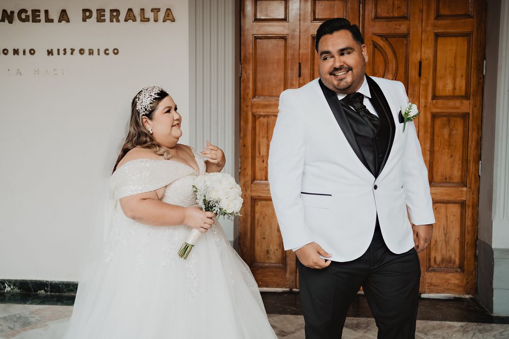 A couple in wedding attire poses in front of wooden doors at Teatro Angela Peralta with playful expressions.