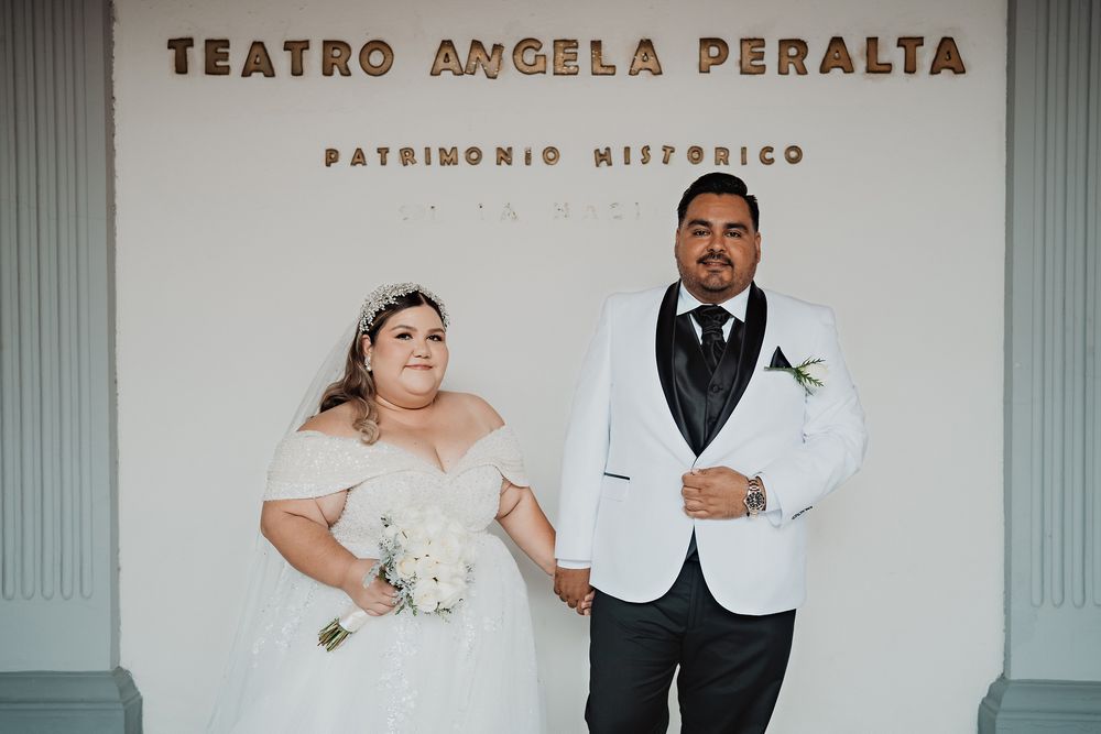 A newlywed couple stands against Teatro Angela Peralta signage in contrasting white wedding attire.