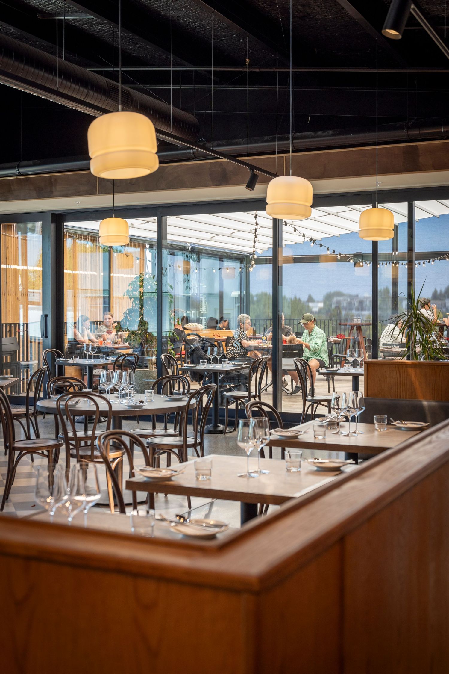 Modern restaurant with warm pendant lighting, glass walls, and guests dining at sunset.