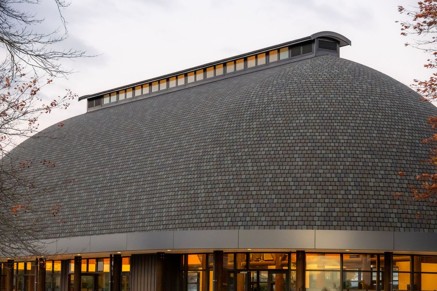 Dome-shaped building exterior clad in dark shingles with warm internal glow.