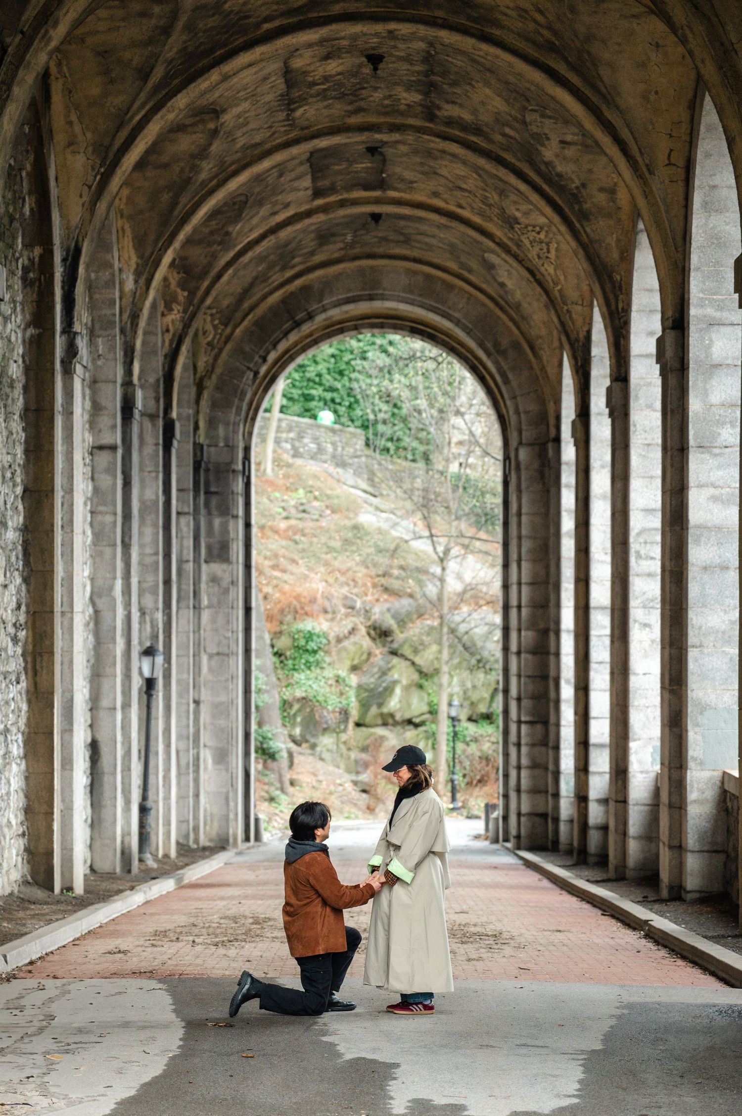 A proposal moment captured under a grand stone archway with arched ceilings and columns in an architectural corridor.