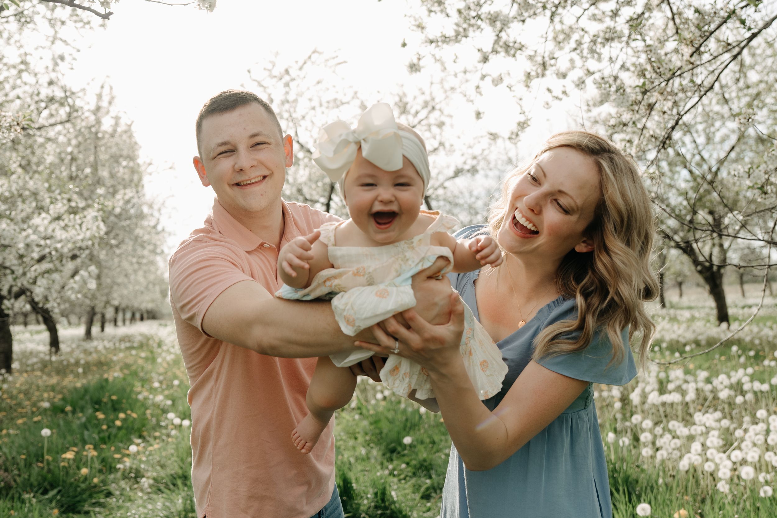 A family enjoys playful moments together in a blooming spring orchard with white flowers.
