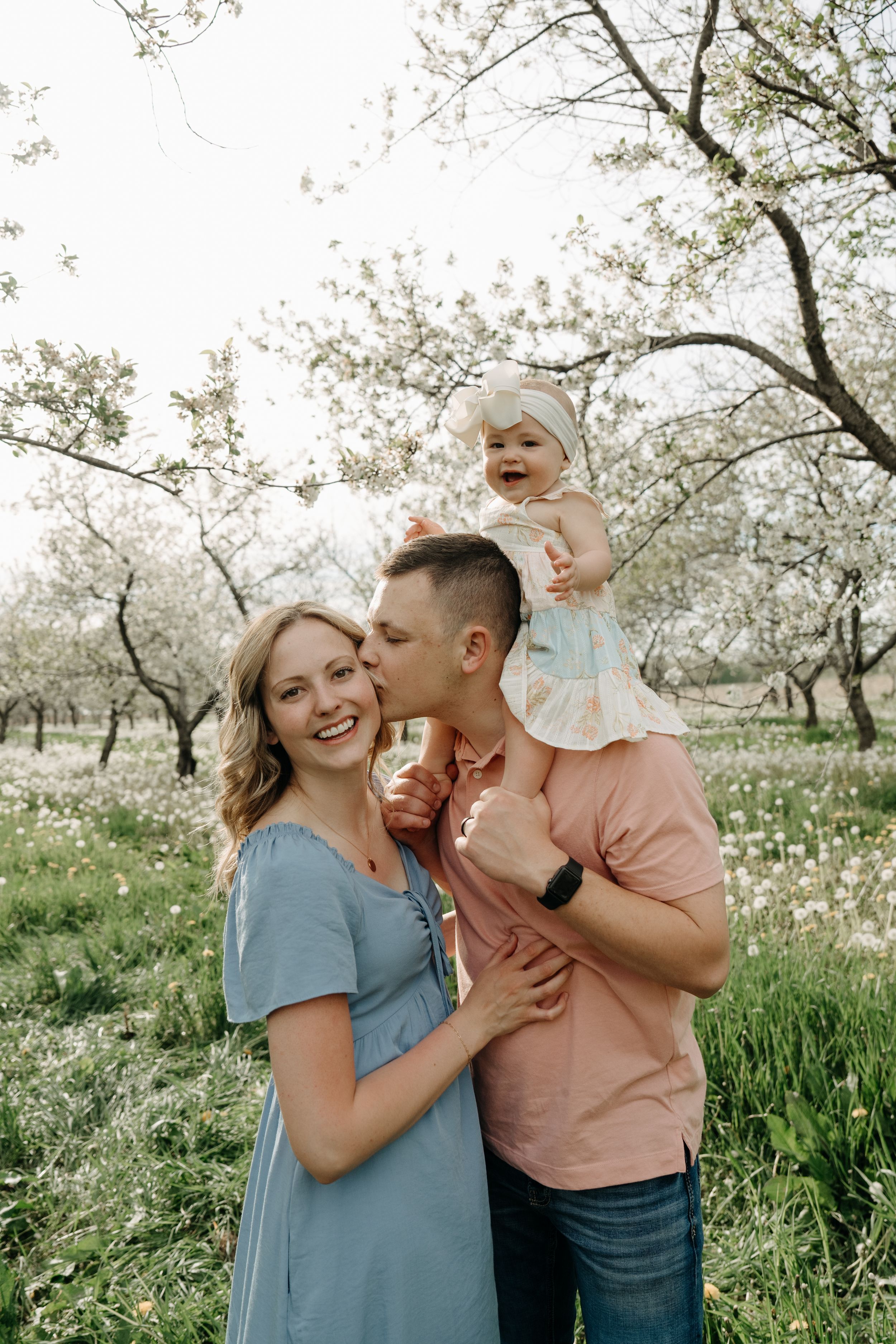 A family enjoys a playful moment together among blooming cherry trees in a spring orchard.