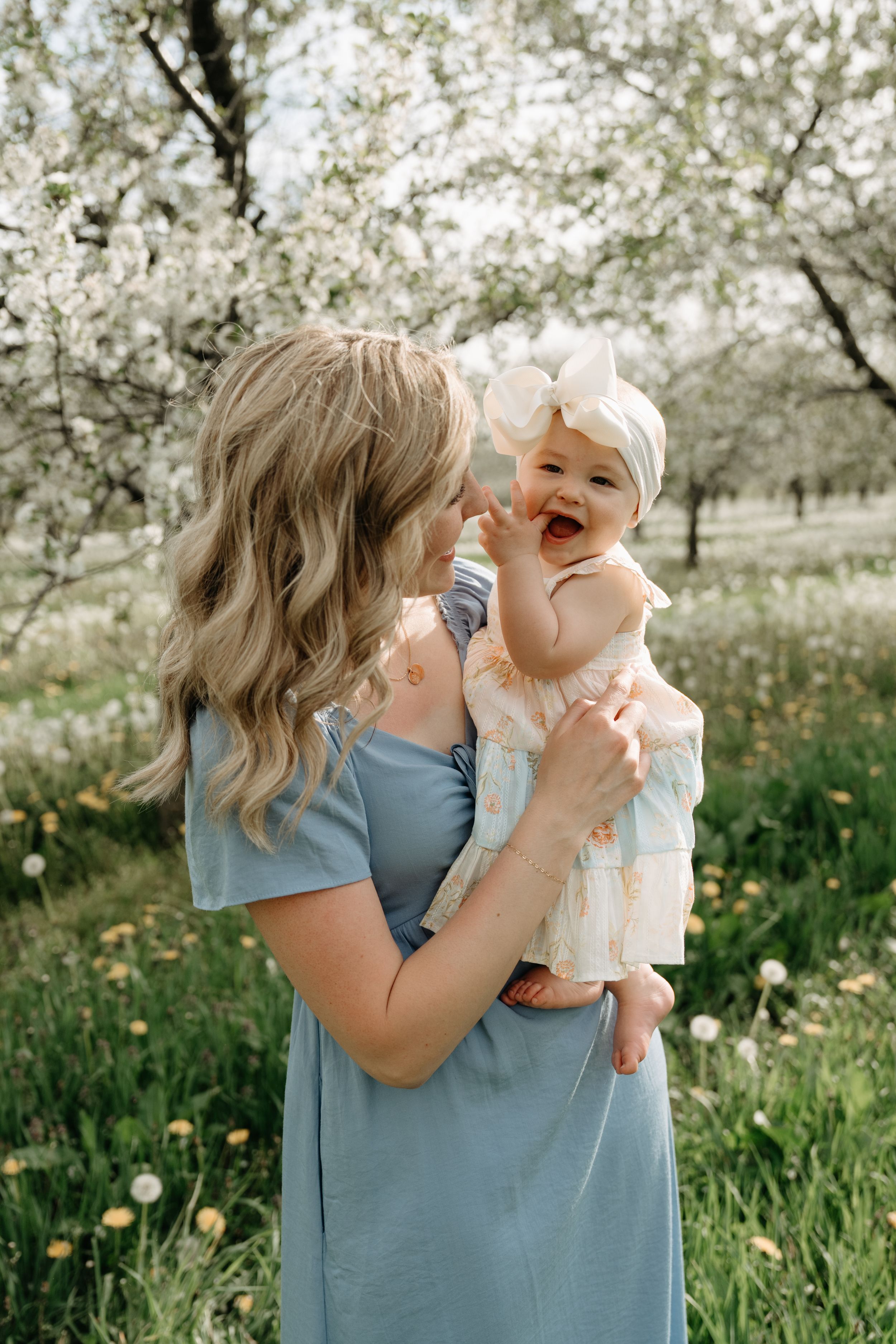 Joyful interactions in a spring orchard with blooming white blossoms as backdrop, wearing soft blue dress and white dress.
