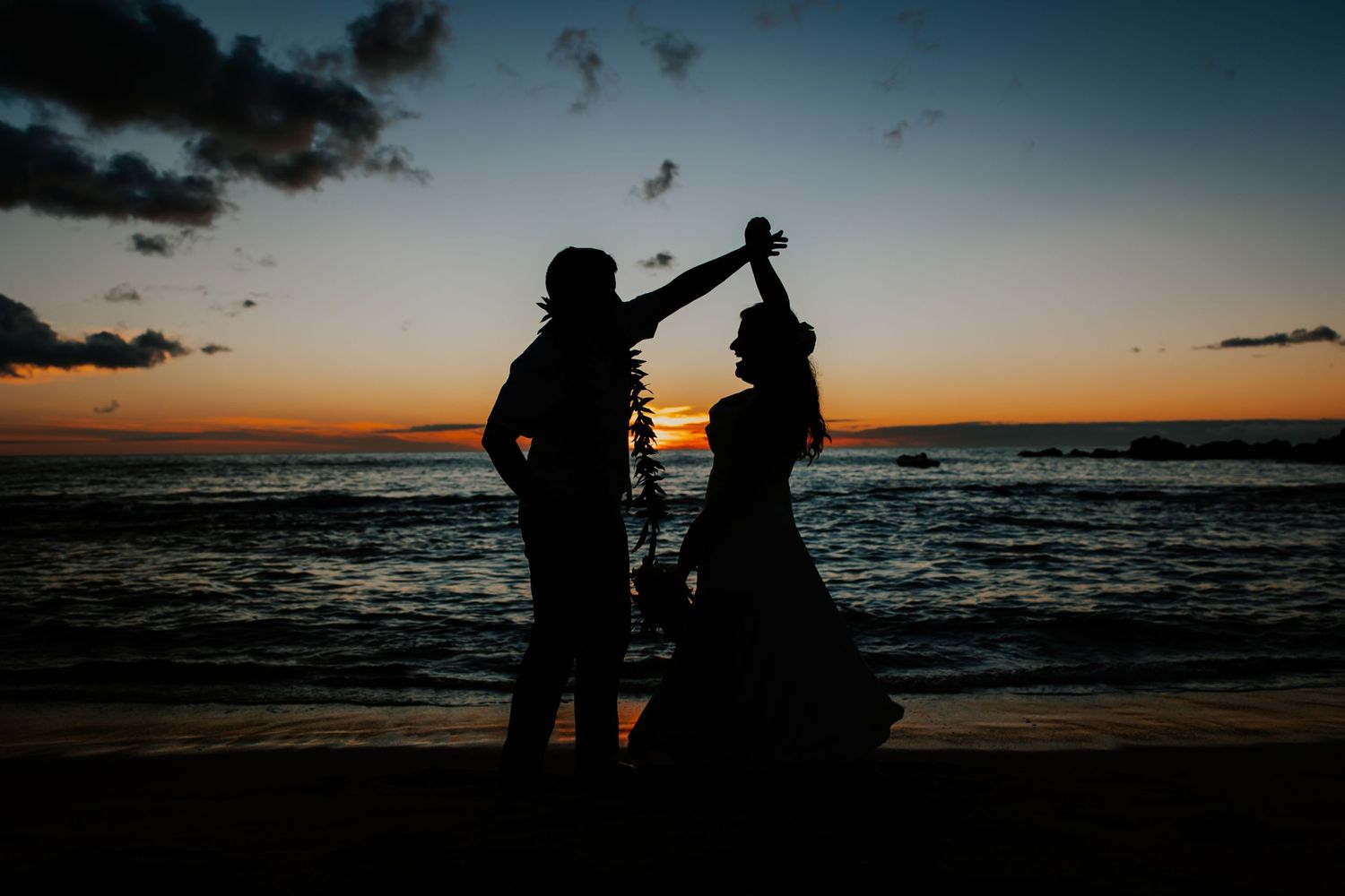 Silhouette of groom spinning bride during their elopement as the sun sets over the ocean on a beach in Hualalai, Hawaii.