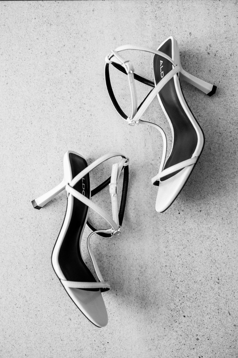 Elegant white strappy high heel wedding sandals on light gray background.