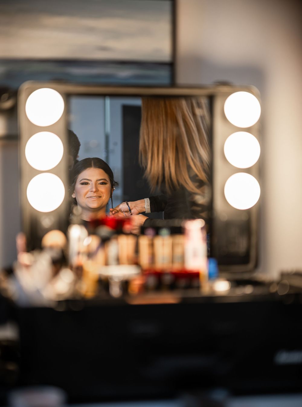 Reflection in illuminated makeup mirror shows beauty preparations with professional lighting and cosmetics setup.