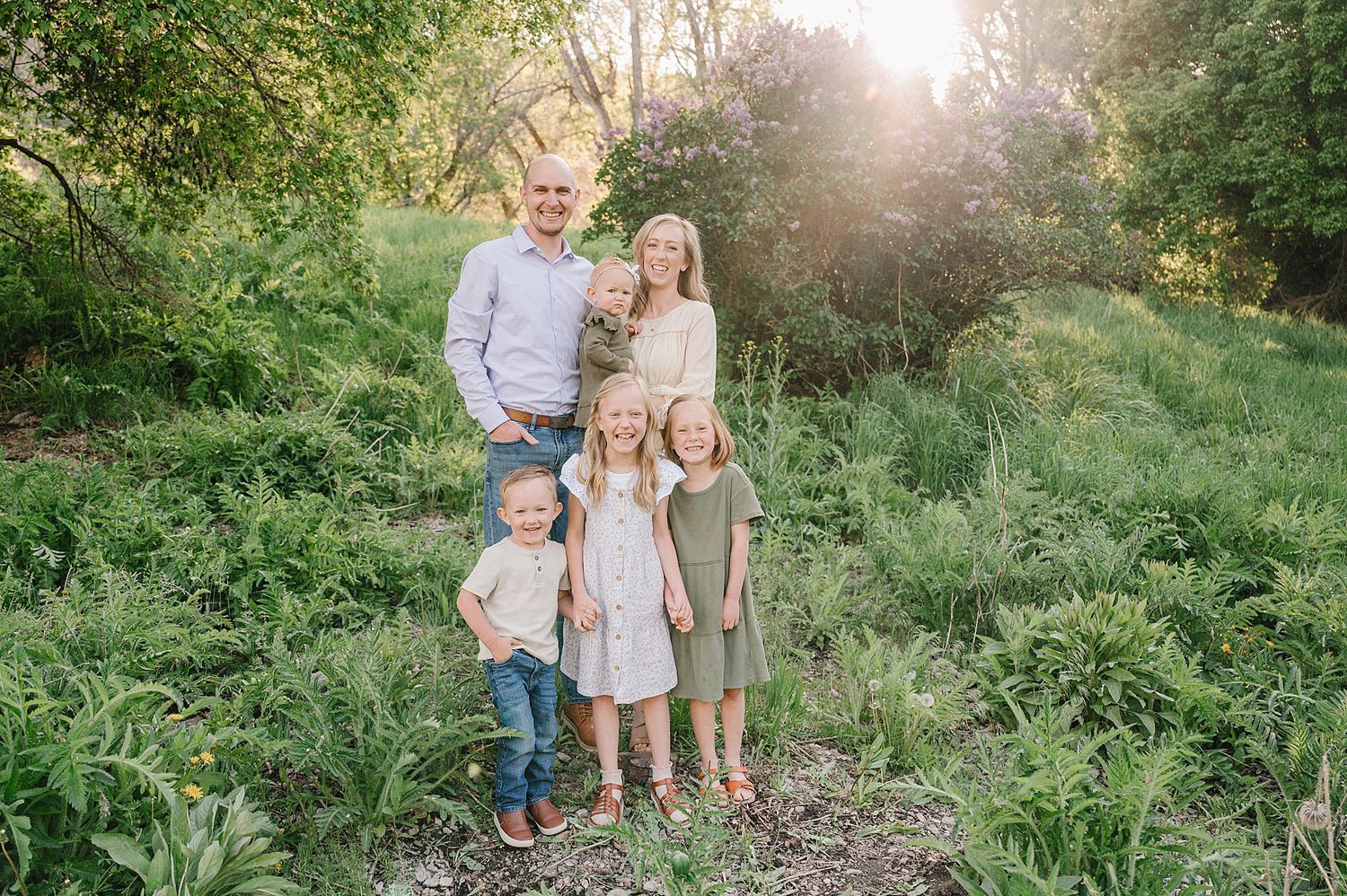 A family stands together on a nature trail surrounded by lush green vegetation during golden hour sunlight.