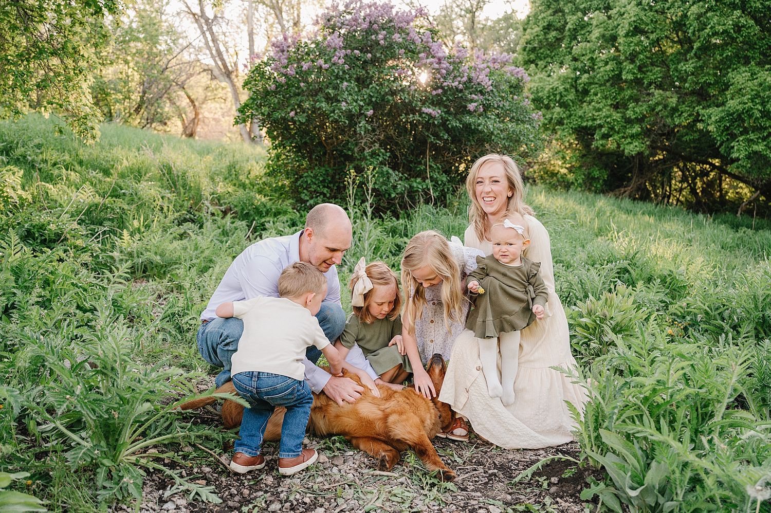 Family and golden retriever dog relaxing together outdoors in a lush natural setting during golden hour.