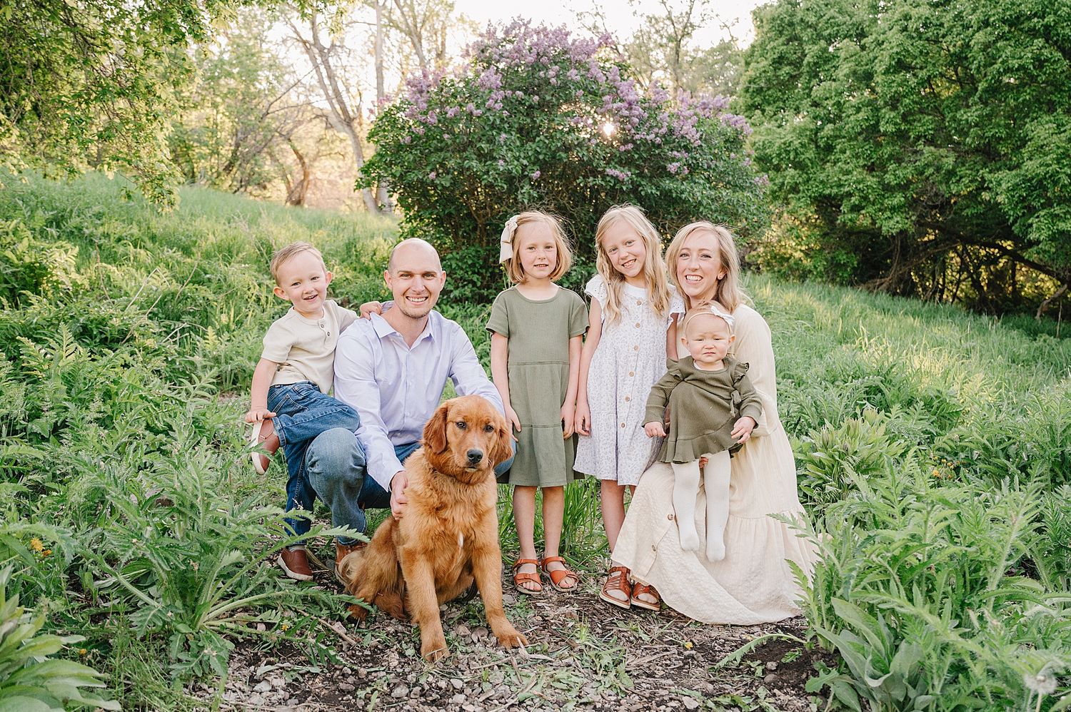 A golden retriever dog sits with a group in a lush green outdoor garden setting during a professional photo session.