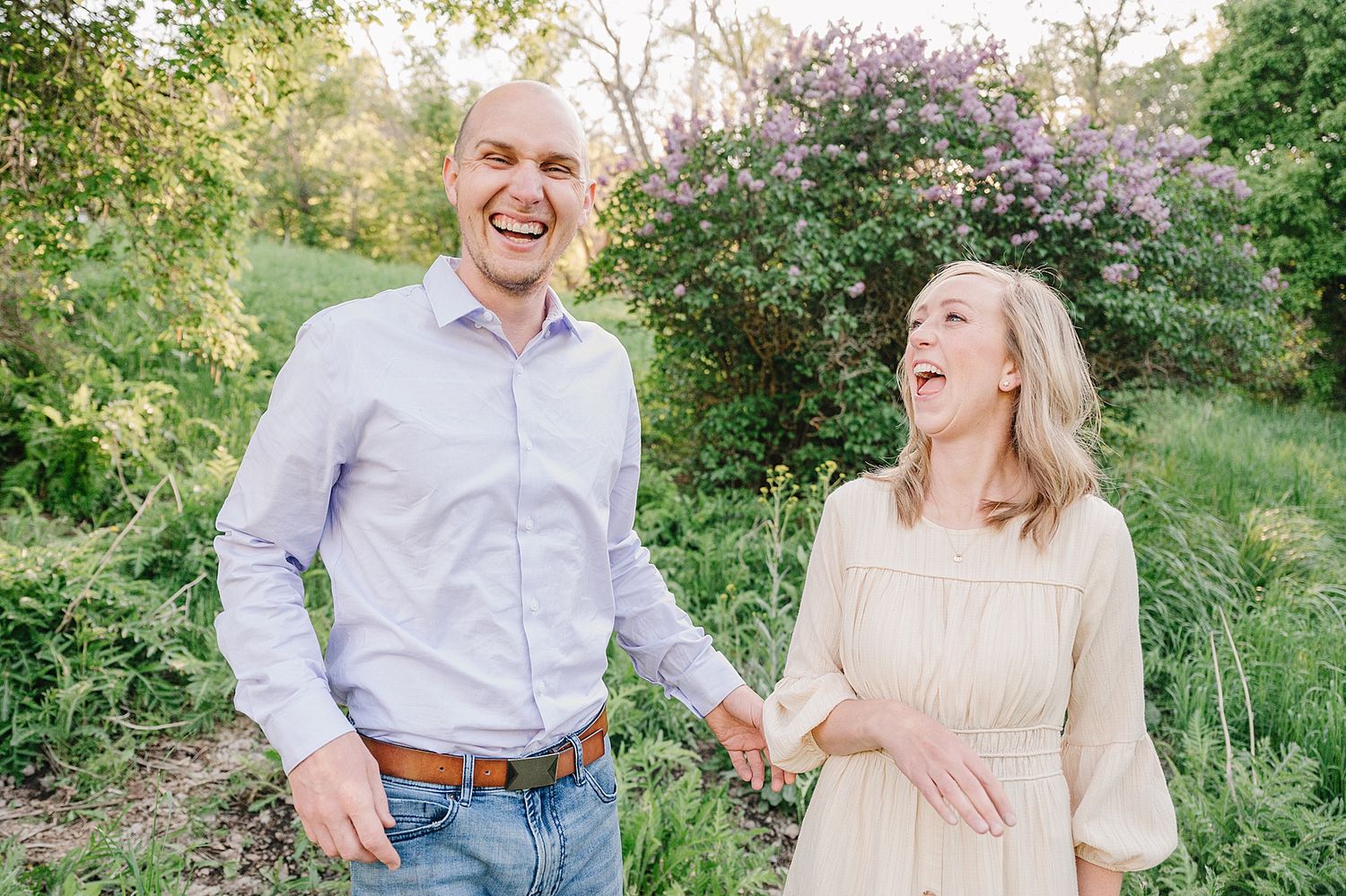 Two people share a joyful candid moment while holding hands in a garden setting with blooming flowers and greenery.