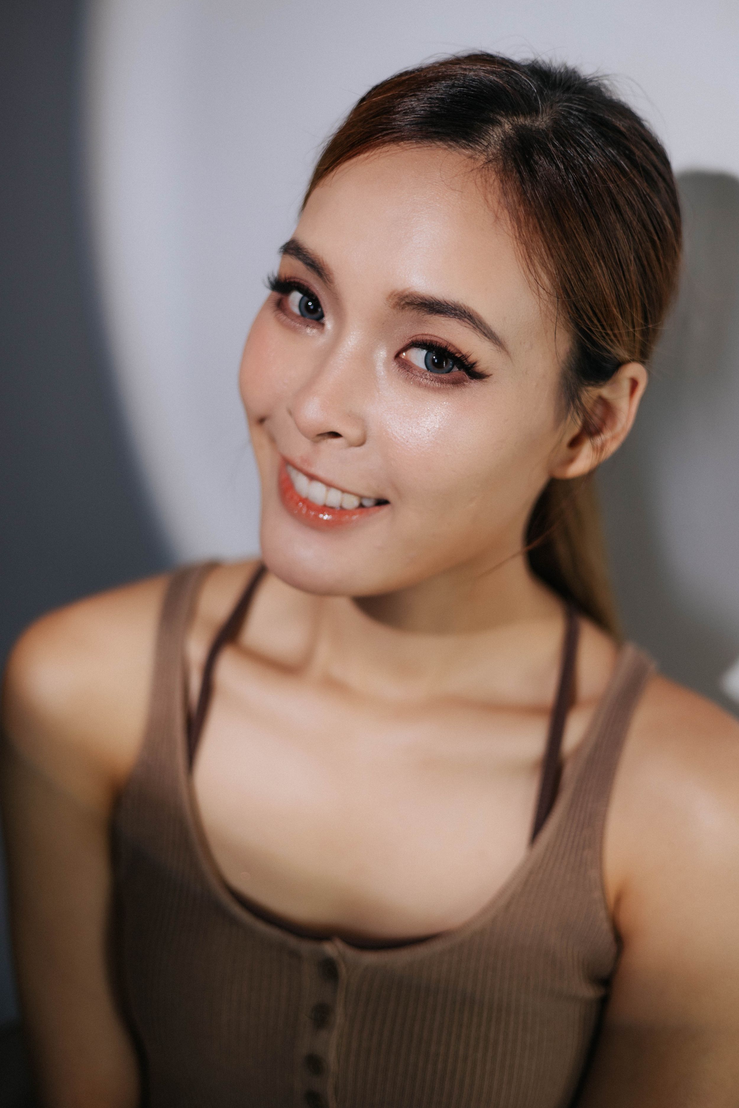 Woman in brown tank top smiling at camera in soft lighting.