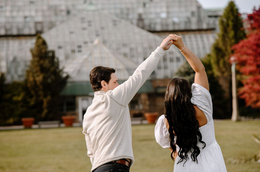 Dancing couple spreads arms wide in joyful celebration on outdoor lawn.