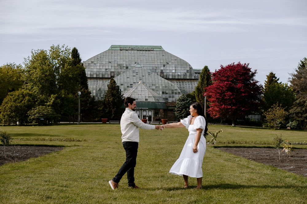 Two people dance together on a lawn with a contemporary glass building and autumn trees behind them.