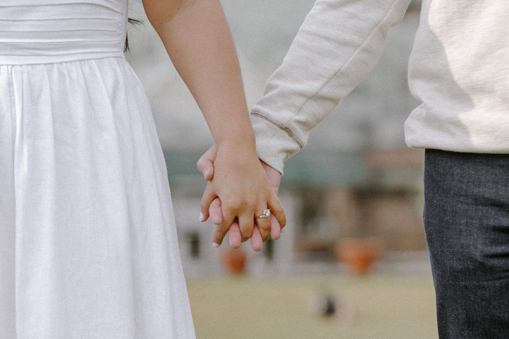 A couple holding hands wearing white and dark clothing against a blurred background.