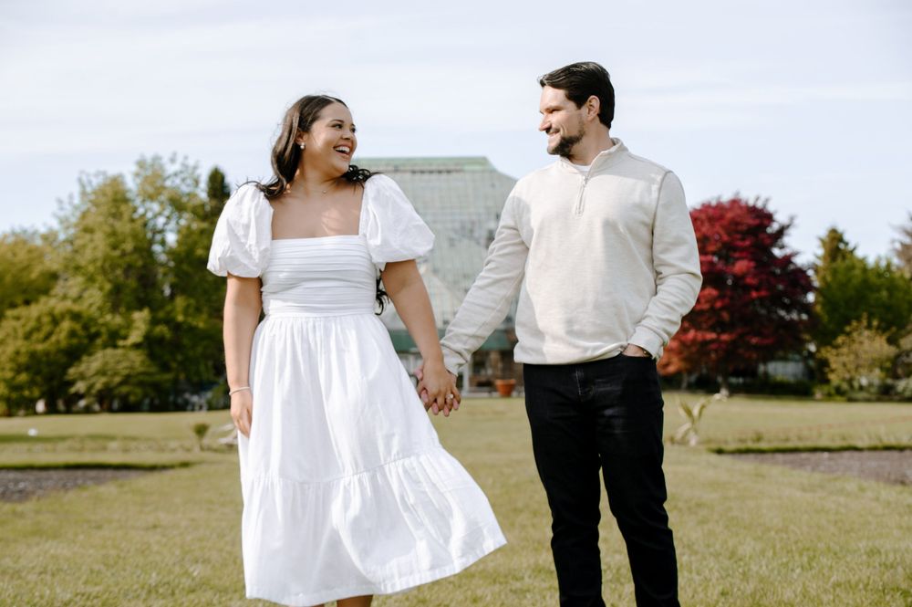 A couple in white and cream outfits share a joyful moment while standing in a grassy field.