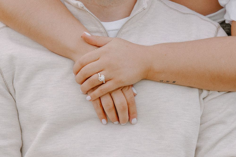 Close-up of hands with engagement ring intertwined on white fabric.